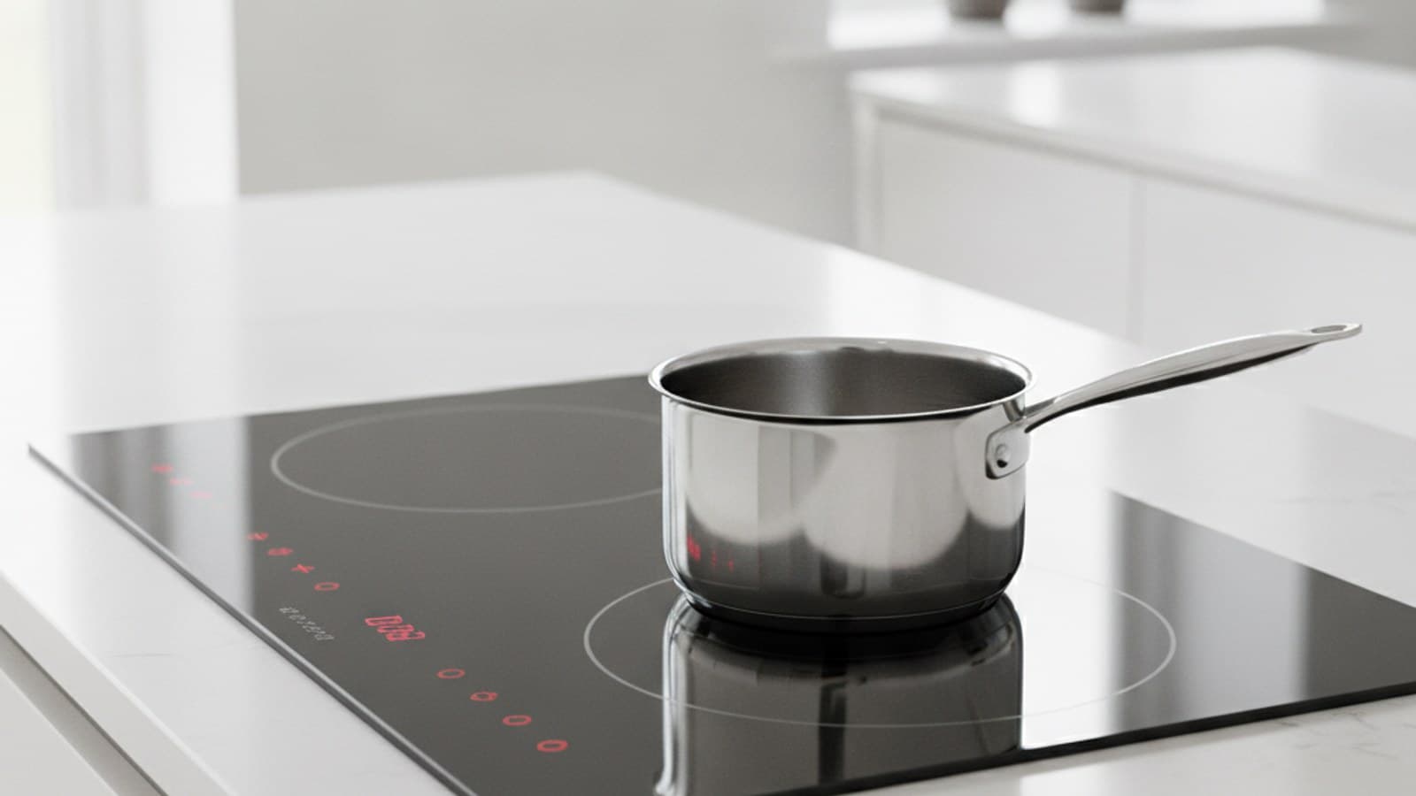 A black glass induction hob set into a white quartz worktop with a stainless steel saucepan on one zone